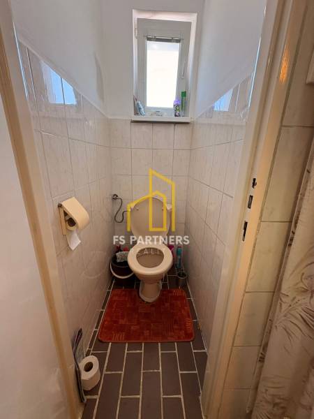 Bathroom of a family house with a toilet, tiles, and a small window.
