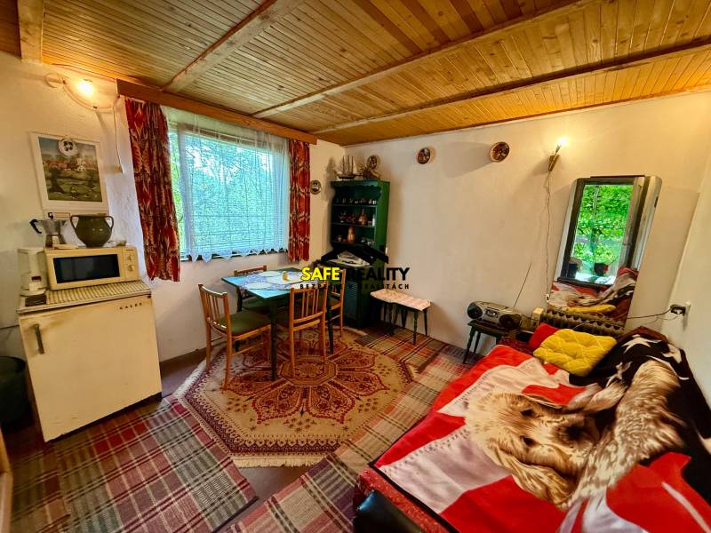 In a cabin with a wooden ceiling, there is a table, chairs, and an antique refrigerator.
