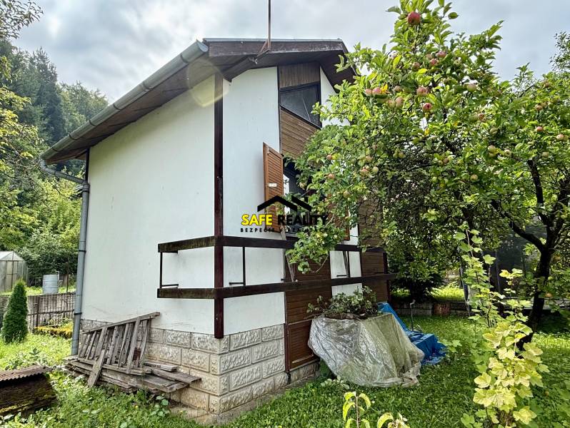 A cottage in Mojš with a fruit tree in the garden and a hill in the background.