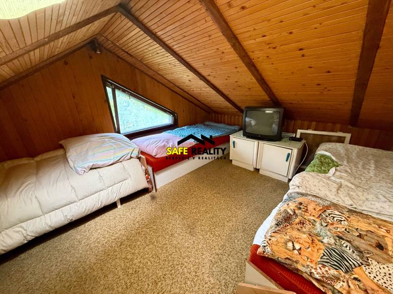 Attic room in a cottage with three beds and a television.