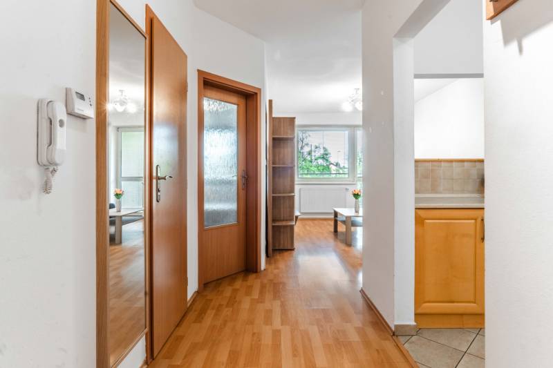 Interior of a 2-room apartment with wooden doors, flooring, and a view of the living room and kitchen.