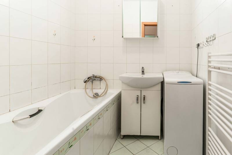 Bathroom with a bathtub, sink, cabinet, and washing machine in a 2-room apartment.