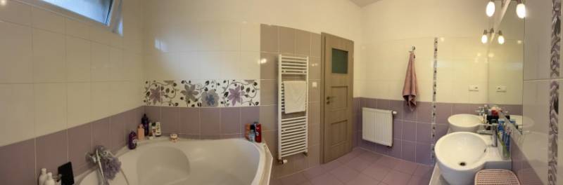 A bathroom in a family house with a wide bathtub, double sink, patterned tiles, and a large mirror.