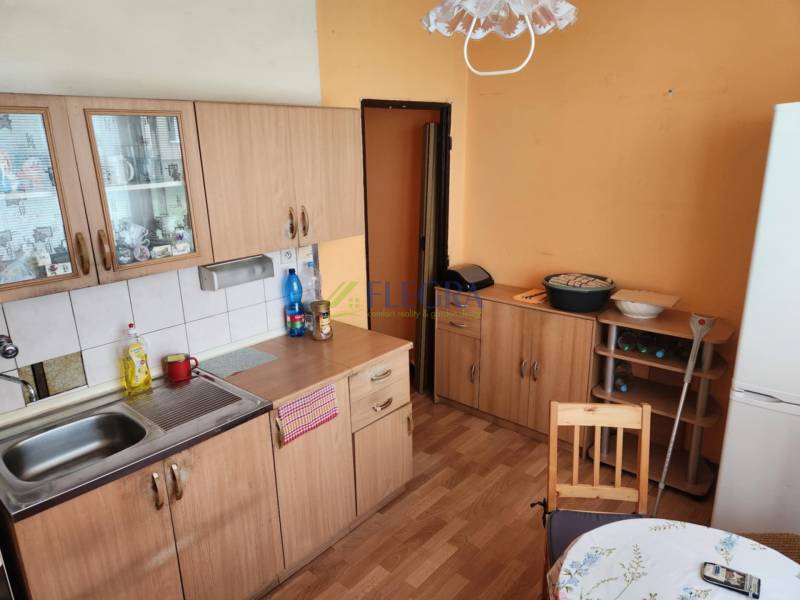 A kitchen in a studio apartment with wooden cabinets, a table, and a refrigerator.