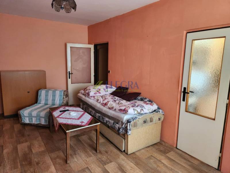 A room in a one-room apartment with a bed, an armchair, and a table on a parquet floor.