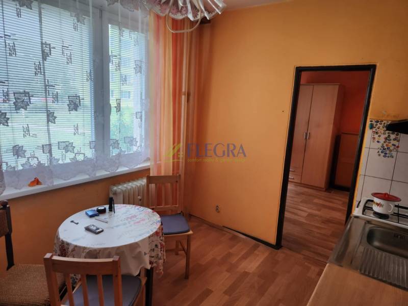 A kitchen in a studio apartment with a table, chairs, and curtains on the window.