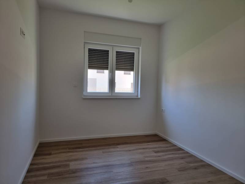A room of a four-room apartment with wooden flooring, white walls, and a window.