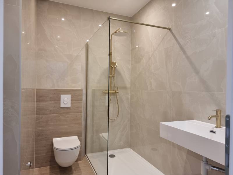 Bathroom in a 4-room apartment with a shower, toilet, and sink, light tiles.