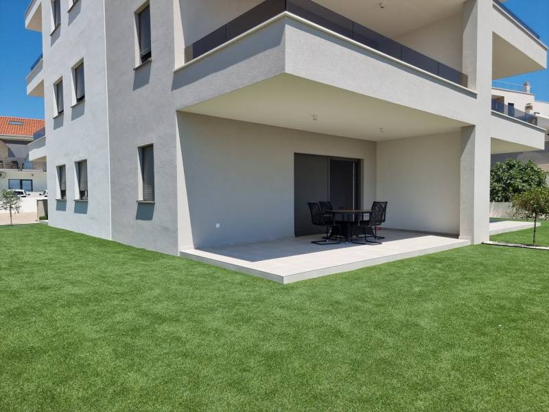 The exterior of a 4-room apartment in Vodice with a modern terrace and green lawn.