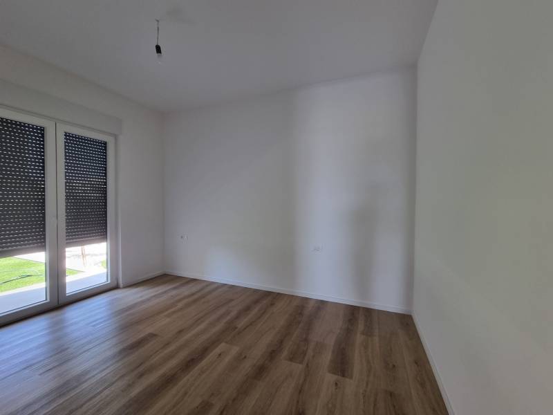 An empty room with wooden flooring and balcony doors in a 4-room apartment.