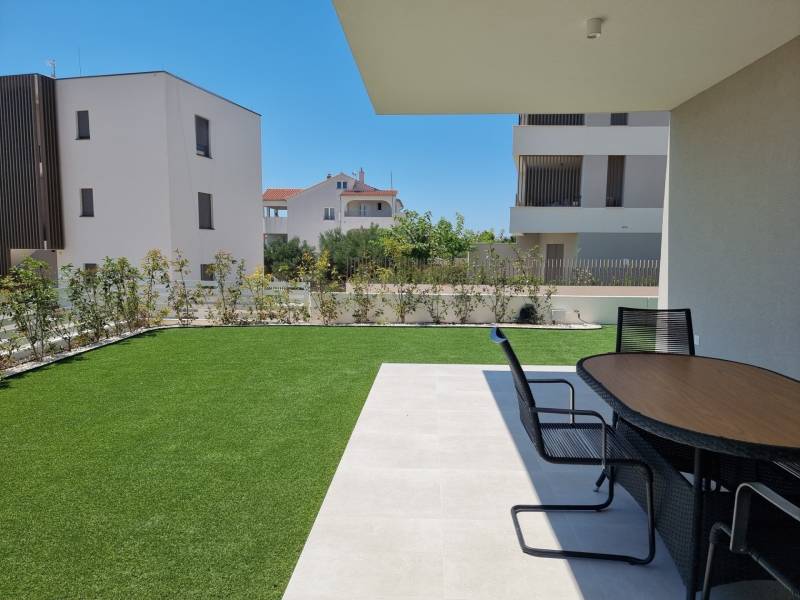 The garden of a 4-room apartment in Vodice with a terrace and a modern table on the grass.