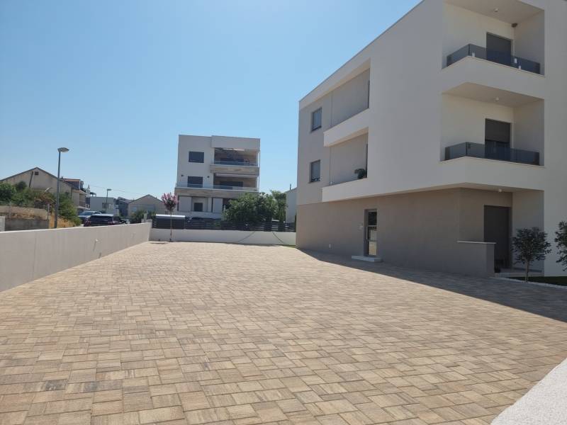 In Vodice, modern apartment buildings and a paved access road are visible.