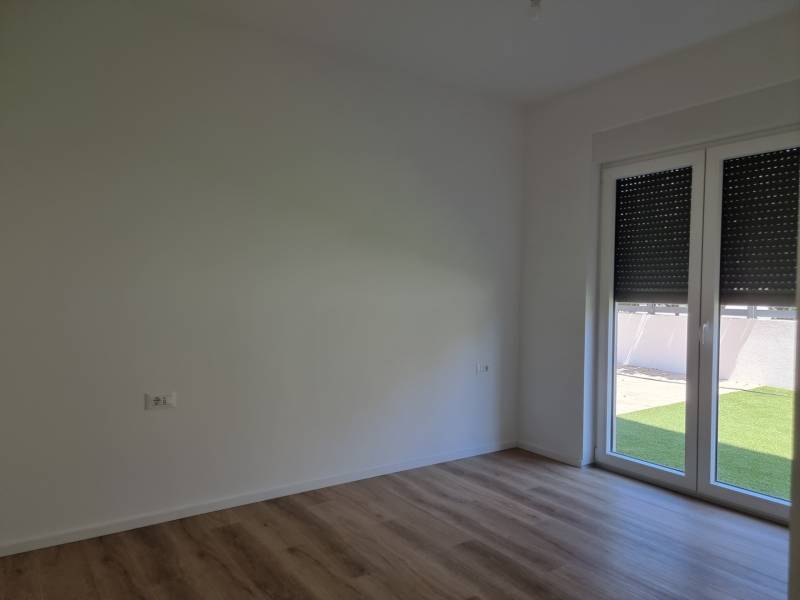 An empty room in a three-room apartment with a wooden floor and a large window.