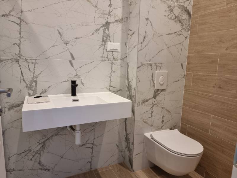 A bathroom with a wall-hung toilet, ceramic sink, and marble tiles in a 4-room apartment.