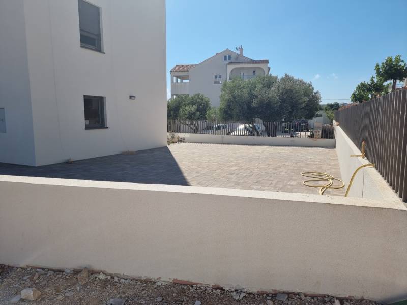 A yard with a 4-room apartment in Vodice with a paved terrace and a low fence.