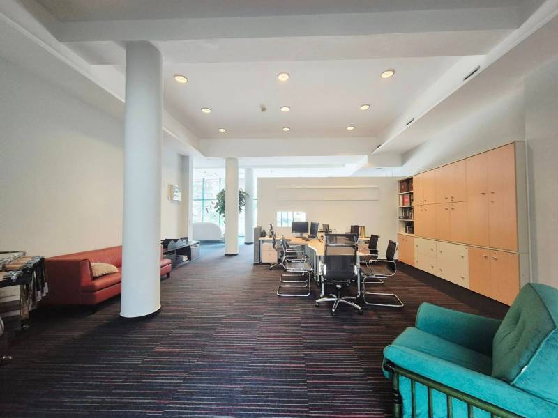 Office space with a large table, chairs, sofas, cabinets, and carpeted floor.