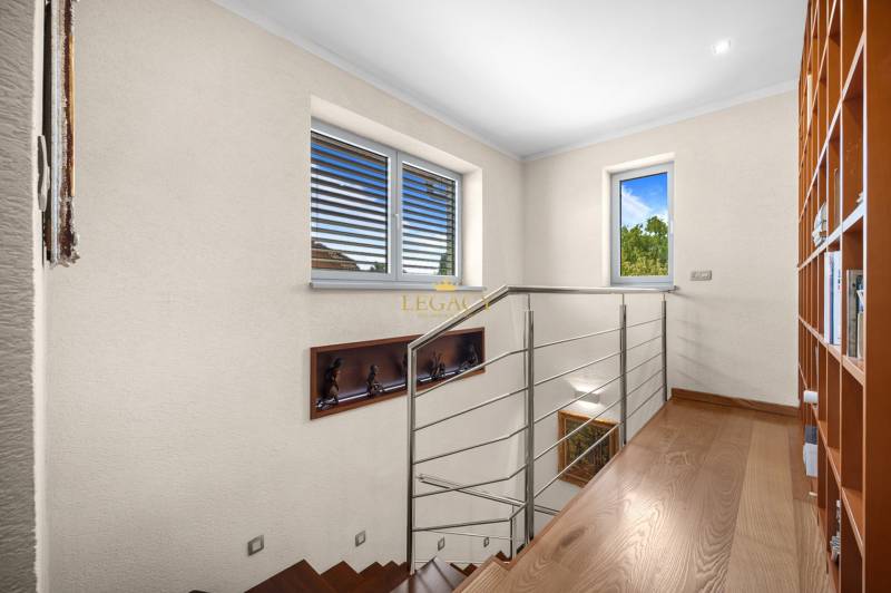 Wooden staircase with metal railing, bookshelf, and windows in a family house.