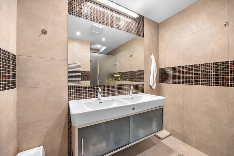 A bathroom with a double sink, brown tiles, and a mirror in a family house.