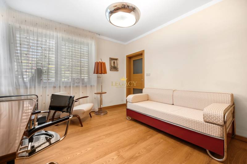 A room in a family house with a sofa, armchairs, a lamp, and wooden flooring.