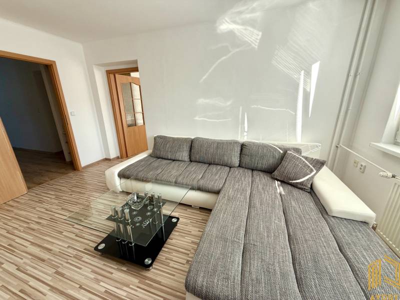 A bright living room with a corner sofa and a glass table in a two-room apartment.