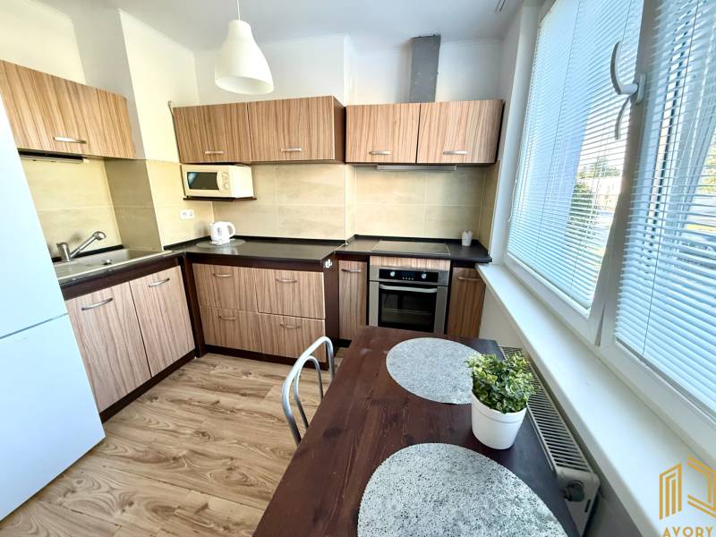 A kitchen in a 2-room apartment with light wood, white appliances, and a table.