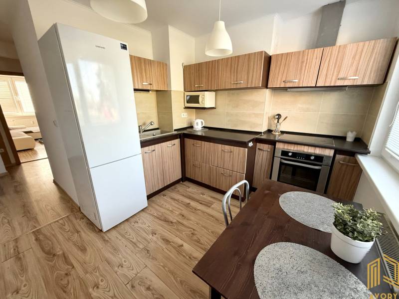 A kitchen in a 2-room apartment with wooden furniture, a white refrigerator, and a dining table.