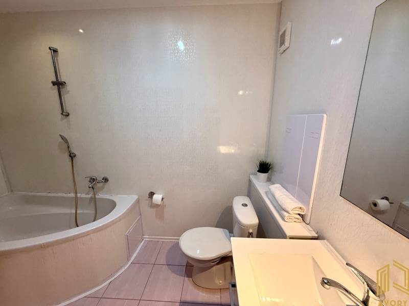 Bathroom in a 2-room apartment with a bathtub, sink, and toilet, light tiles.