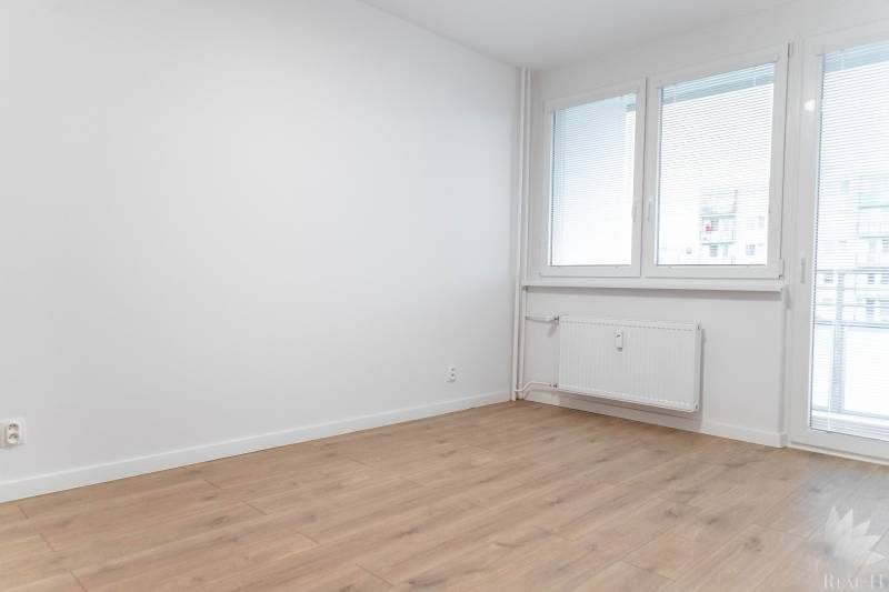 A room with a wooden floor, walls, and large windows in a 2-room apartment.