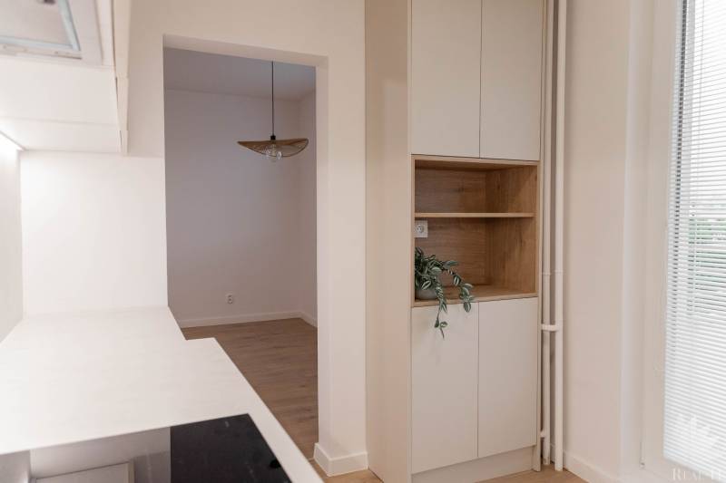 Interior of a 2-room apartment with a white kitchen and wooden shelves.