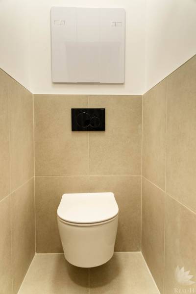 Wall-hung toilet in a 2-room apartment, beige tiles, black flush button.