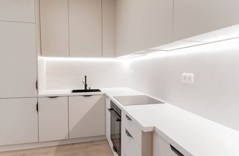A kitchen in a 2-room apartment with white cabinets and a black sink.