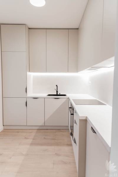 A kitchen in a 2-room apartment with light cabinets and lighting above the countertop.