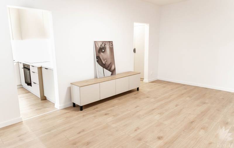 A room in a 2-room apartment with wooden flooring and furniture, next to the kitchen.