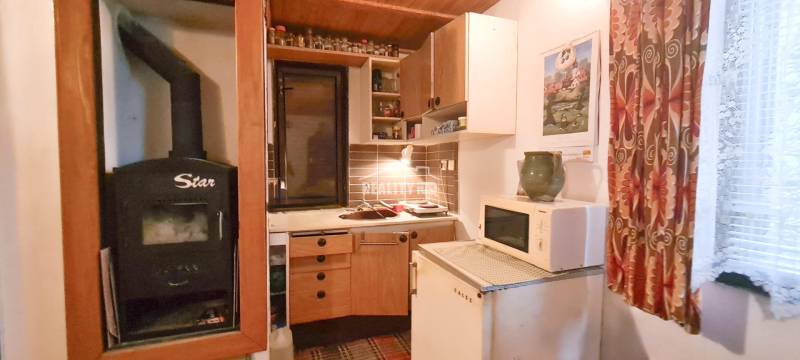 A cottage with a kitchen, stove, microwave, heating, curtains, cabinets, and wall decorations.