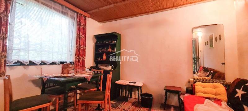 The interior of a cabin with a wooden ceiling, table, chairs, and a shelf.