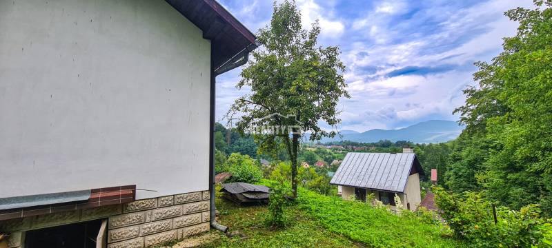 The view from the cottage in Mojš shows roofs, greenery, and distant hills under a cloudy sky.