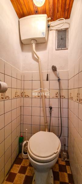A small bathroom in a cottage with a toilet, tiles, and a wooden ceiling.