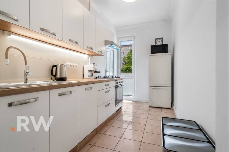 A kitchen with white cabinets, appliances, and a window in a two-room apartment.