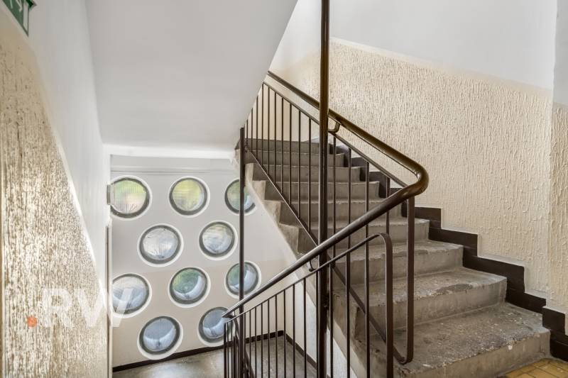 Staircase with railing, round windows, textured walls, spatial arrangement.