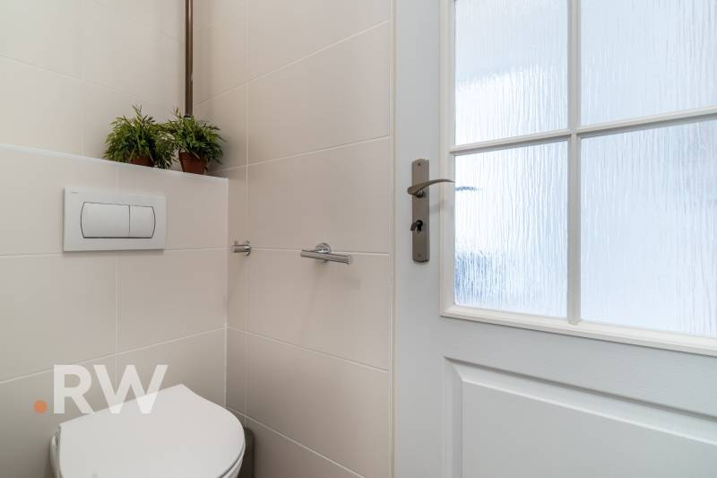Bathroom of a 2-room apartment with a toilet, ceramic tiles, and glass doors.