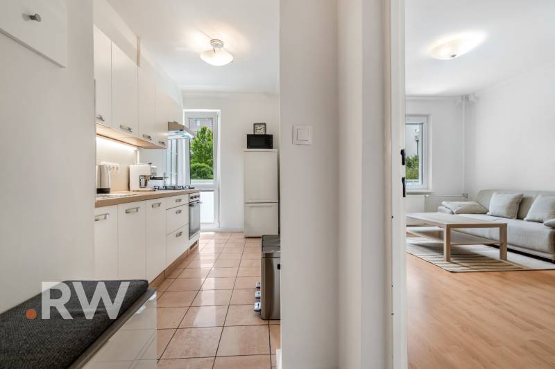 The kitchen with white cabinets transitions into the living area with wood-patterned flooring.