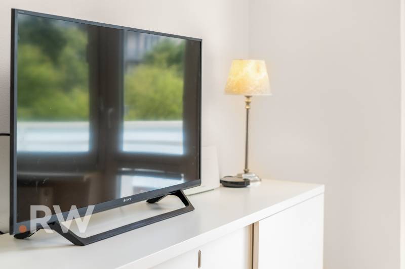 A television and a lamp on a white dresser in a 2-room apartment.