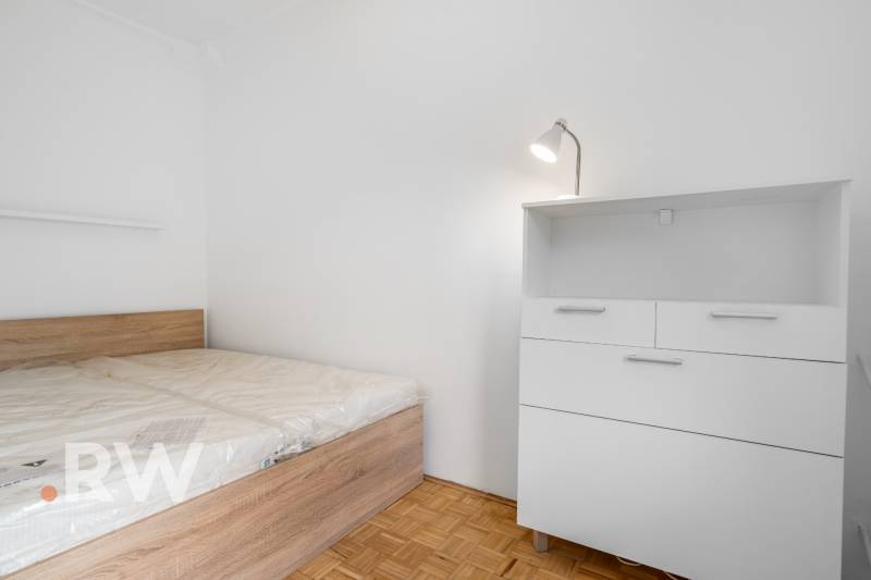 Bedroom with a bed and a dresser in a 2-room apartment, floor with wooden decor.