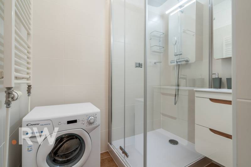 Bathroom in a 2-room apartment with a washing machine, shower, and white tiles.