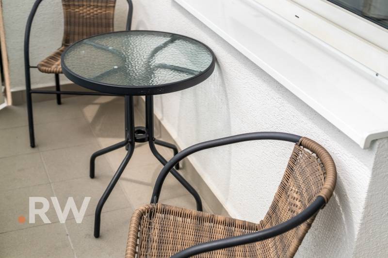 A balcony with rattan chairs and a glass table in a 2-room apartment.