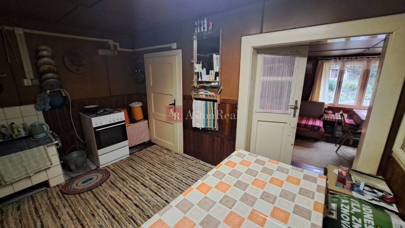 Interior of a cabin with a kitchen, stove, table, and a view into the living area.
