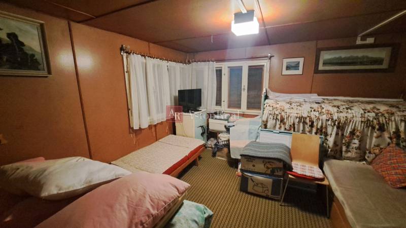 A room in a cottage with beds, a television, paintings on the walls, and a carpeted floor.