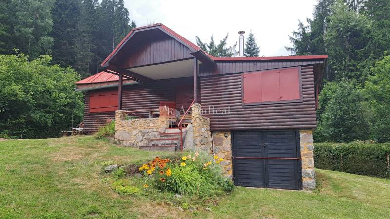 A wooden cottage in Nižné Matejkovo in Ružomberok surrounded by a forest with a flower bed.