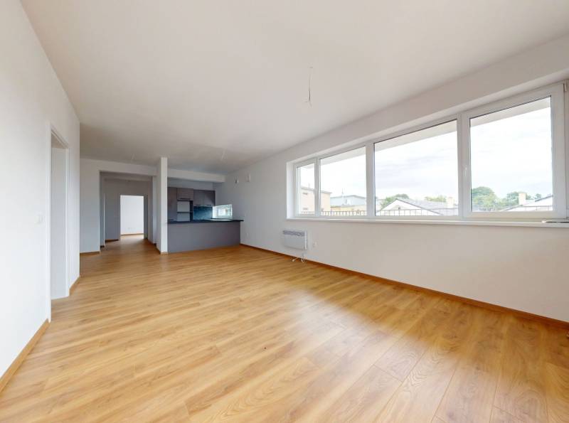 A spacious living room with wooden flooring and large windows in a 3-room apartment.