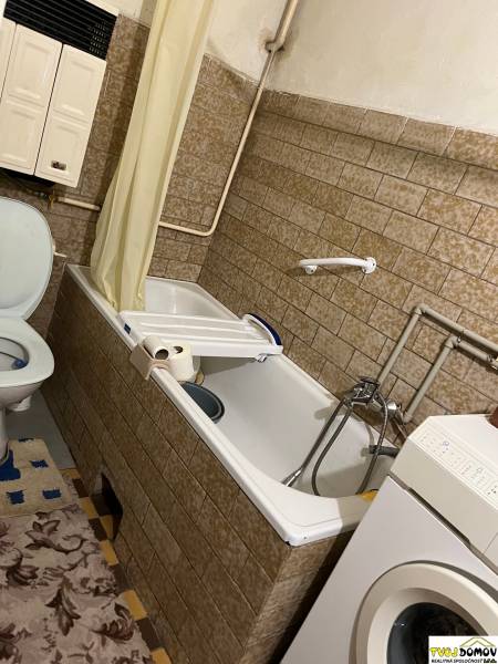 Bathroom in a family house, with a bathtub, washing machine, and tiles.